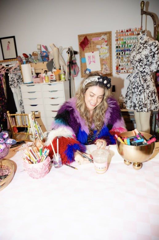 Amanda Perna sketching at a table in the atelier wearing a colorful fur jacket