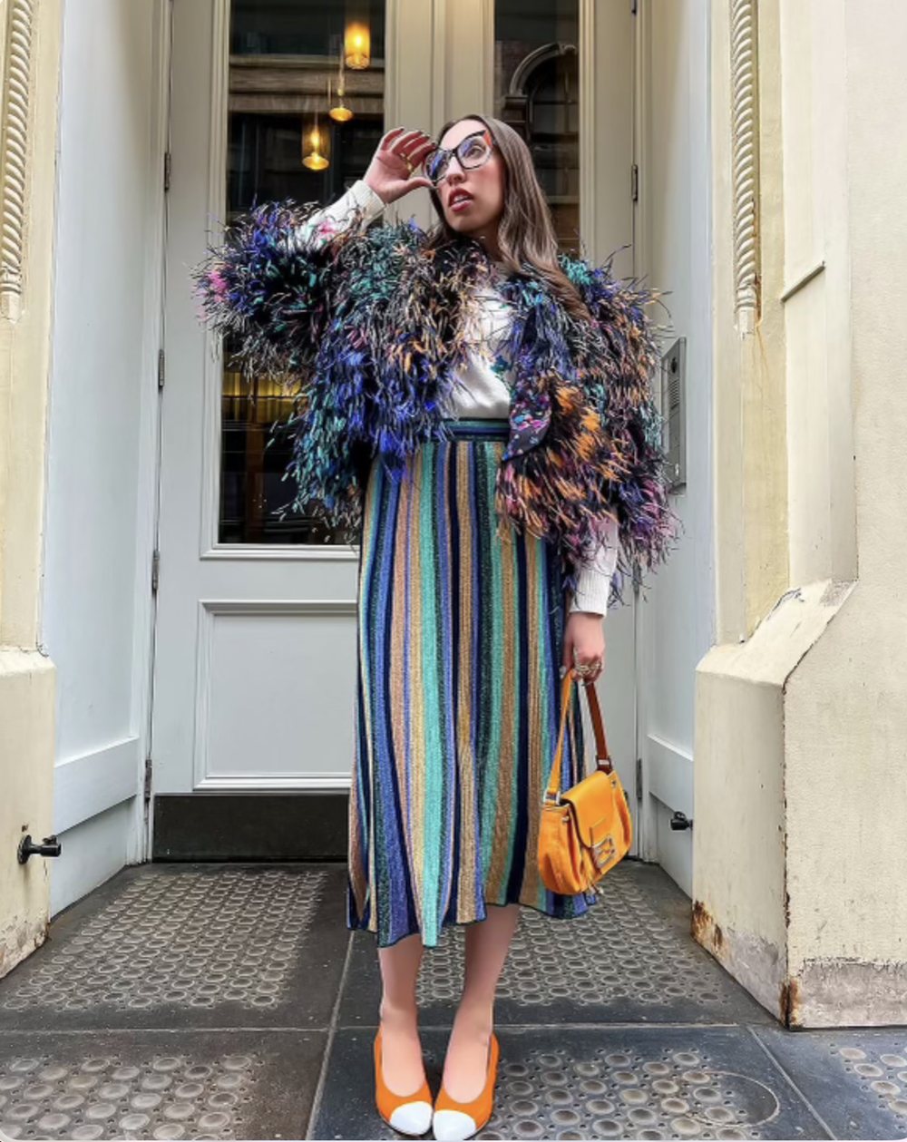 A woman in a multicolor feather jacket and metallic striped skirt in a doorway