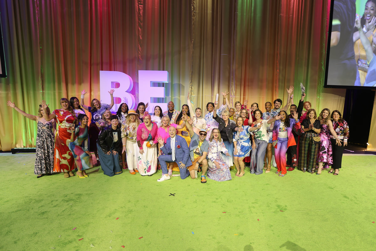 A large group of women celebrating on stage in front of a BE sign
