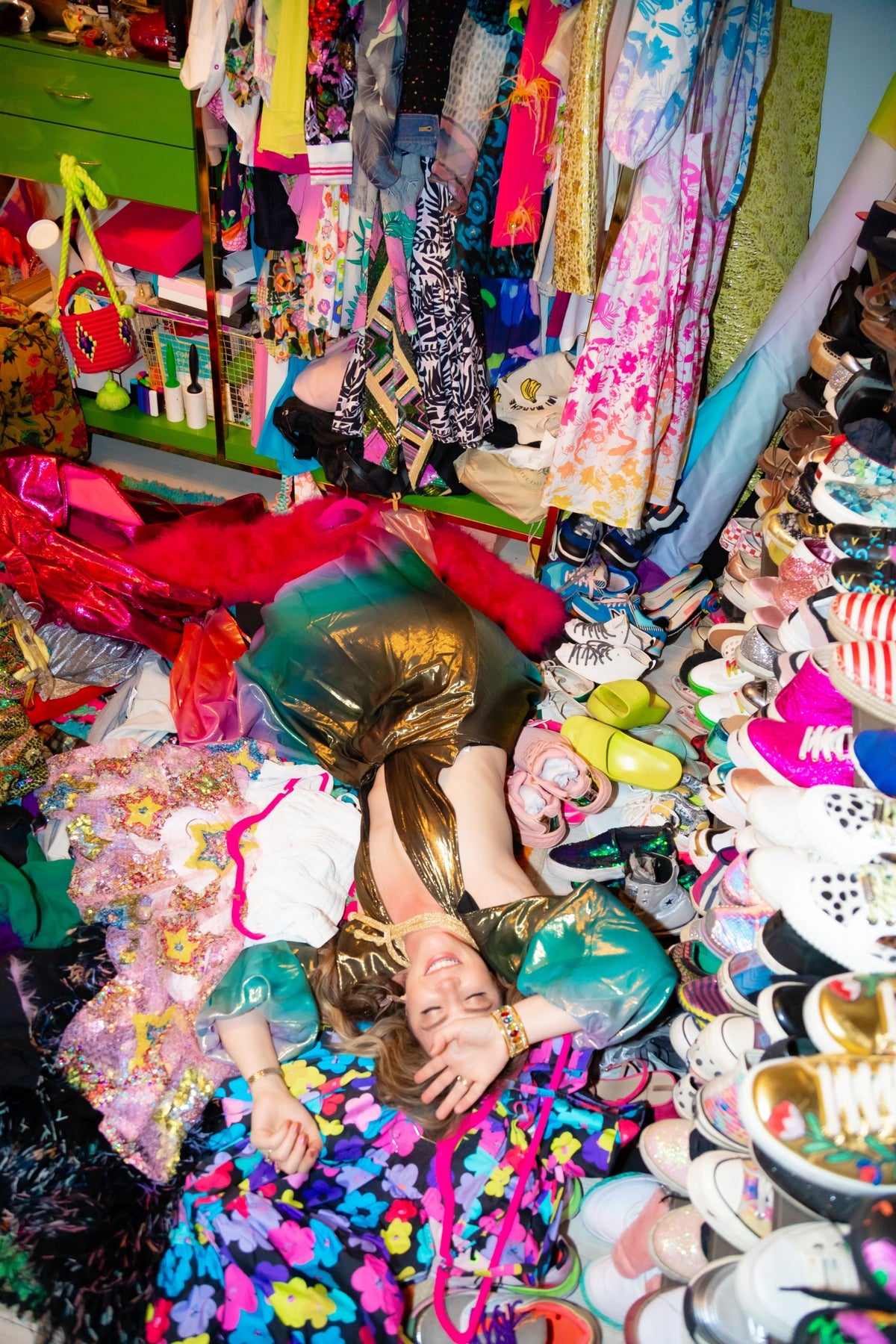 Amanda Perna laughing on a pile of colorful clothes and shoes in a gold metallic dress